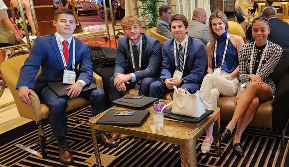 Students wear professional attire and sit on couches at a conference.