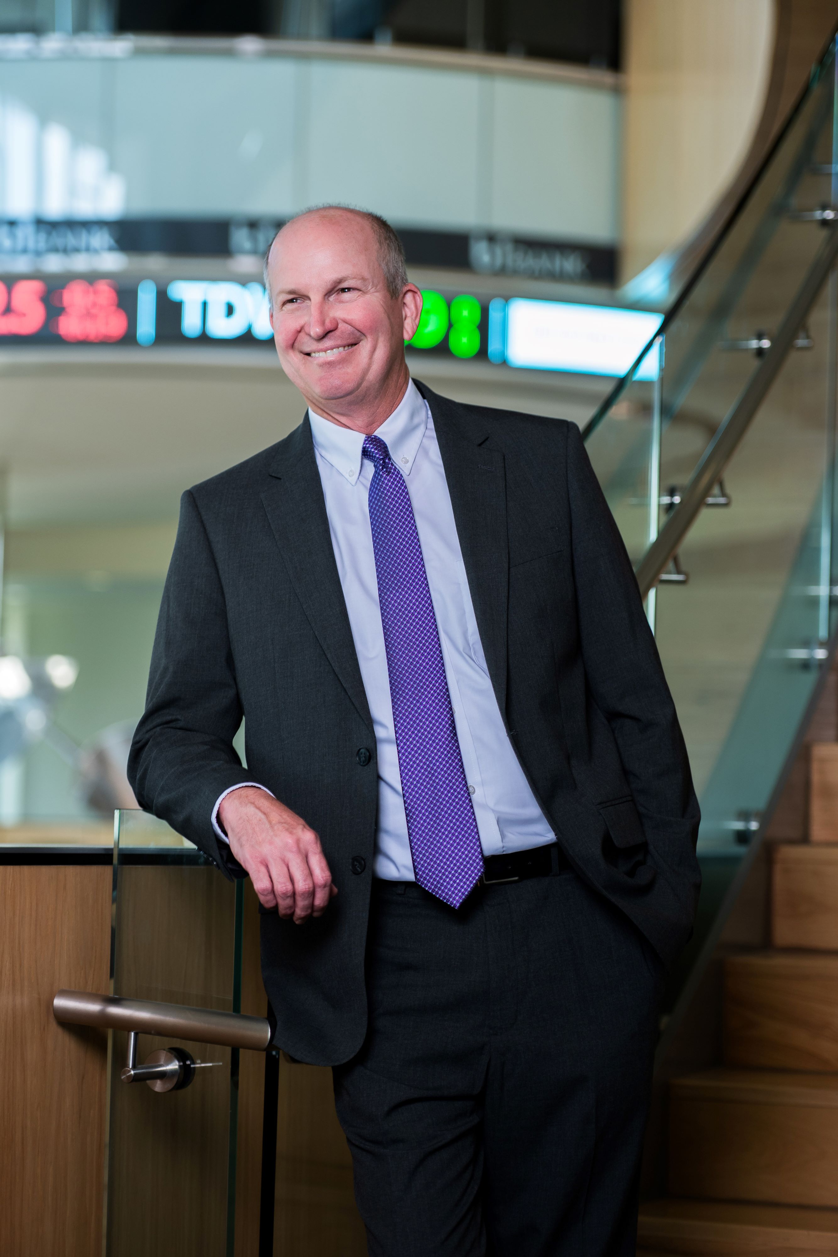Russell Crook leans on balcony in front of a stock ticker 