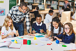 Photo of a male teacher helping students with a geometry project.